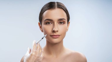 Genç beyaz kadın elmacık kemiklerine kozmetik enjekte ediliyor.