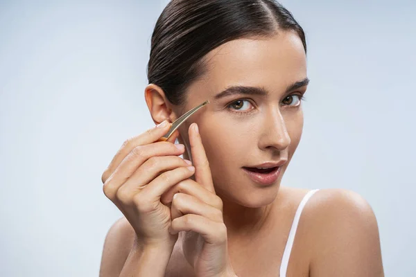 Young Caucasian lady using pliers on her eyebrow — Stock Photo, Image