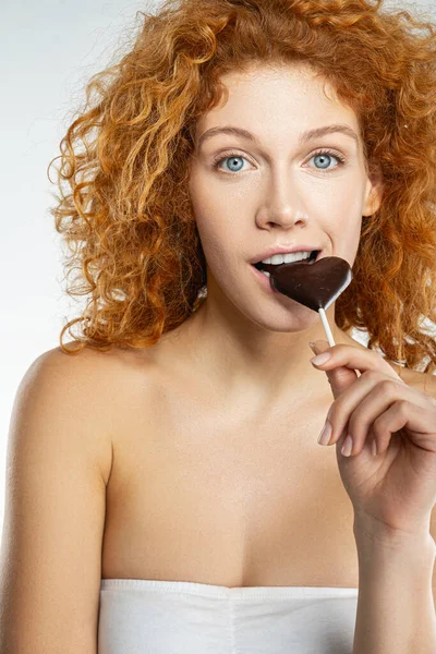 Beautiful woman biting into heart shaped chocolate — Stock Photo, Image