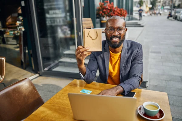 Persona masculina de piel oscura agradable demostrando bolsa de papel — Foto de Stock