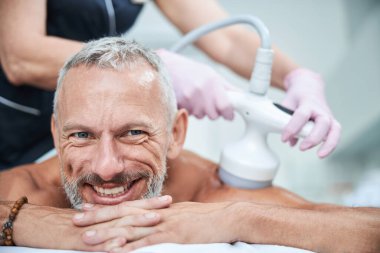 Kozmetik ameliyatlar sırasında sırıtan yaşlı vatandaş yüzüstü yatıyor.