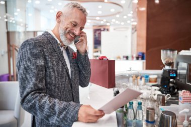 İyi giyimli yaşlı adam telefondayken gülümsüyor.