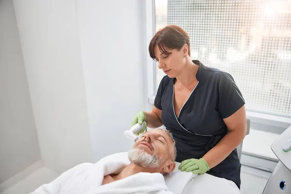 Осторожный косметолог проводит лечение кожи для стареющего мужчины — стоковое фото