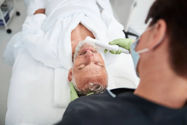 Esthéticienne professionnelle effectuant un traitement photofacial de la peau pour un homme âgé — Photo