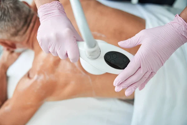 Beautician het bedienen van een massage machine tijdens het behandelen van een man — Stockfoto