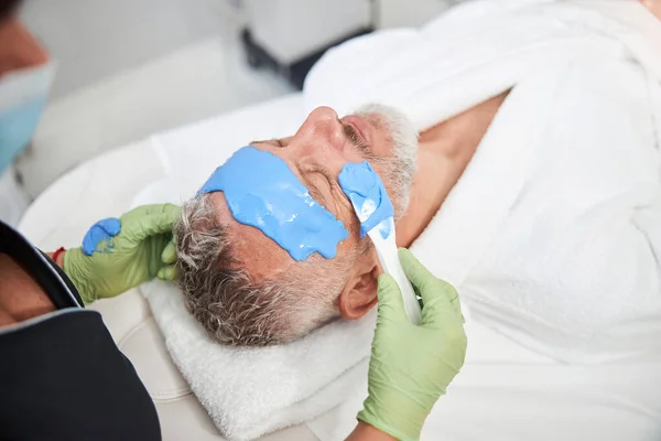 Aging male client of a spa salon enjoying a face mask — Stock Photo, Image