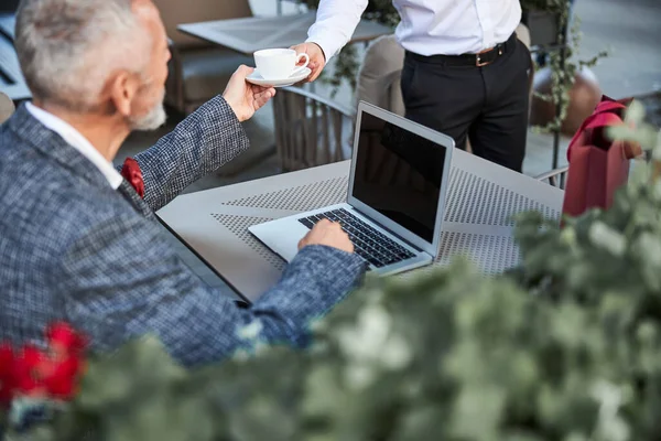 Aging man taking a cup of coffee from a waiter — Stock Photo, Image