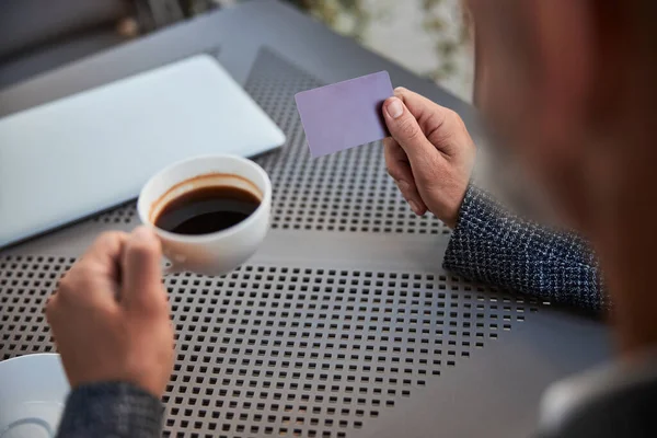 Taza de café y una tarjeta de plástico en las manos del hombre —  Fotos de Stock