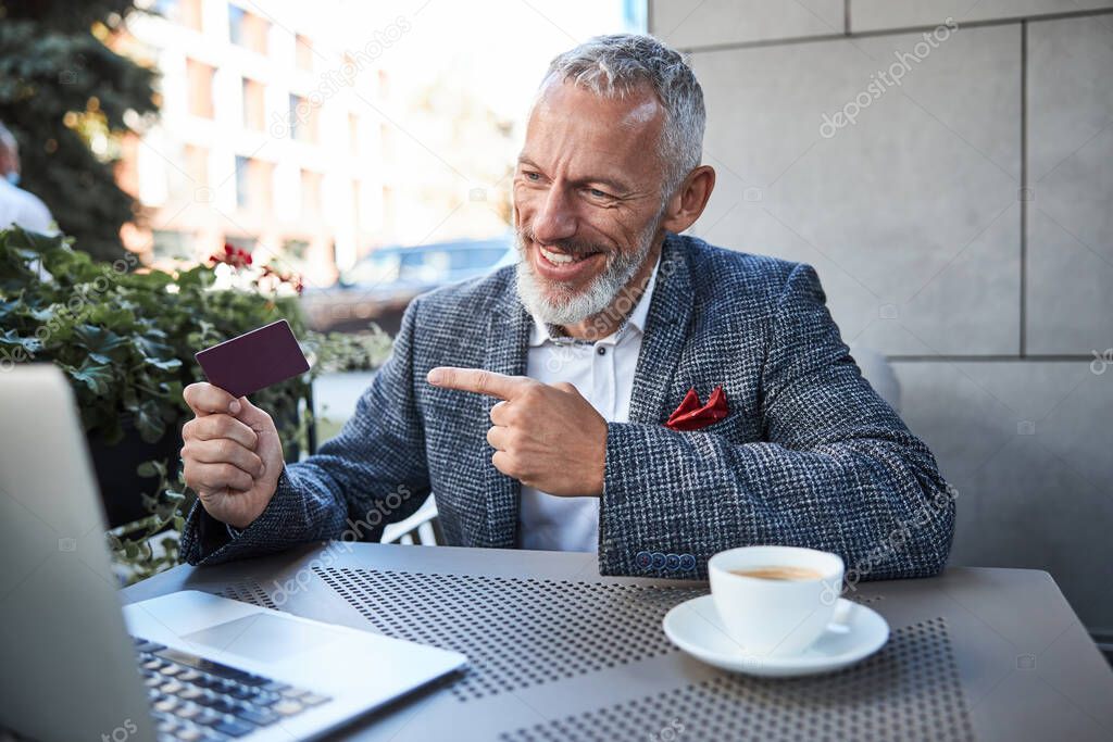 Gladsome senior gentleman demonstrating a card on a videocall