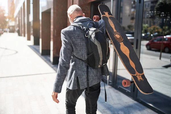 Elegante eldelry homem segurando um longboard e andando — Fotografia de Stock