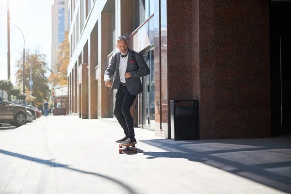 Active elderly gentleman is riding his longboard — Stock Photo, Image