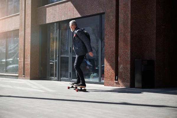 Stylish gentleman riding a longboard through the street — Stock Photo, Image