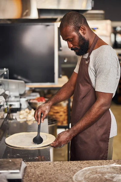 Jeune homme barbu faisant de la pizza dans la cuisine du café — Photo