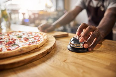Afro-Amerikalı adam pizzacıda servis zilini çalıyor.
