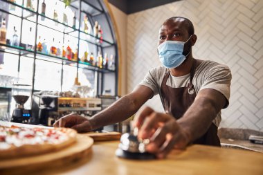 Sağlık maskeli erkek işçi pizzacıda servis zilini çalıyor.