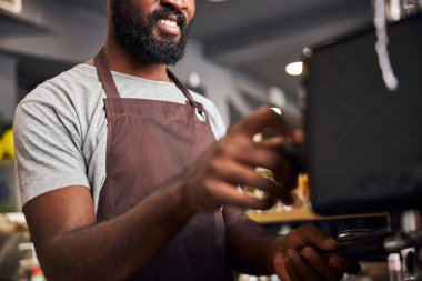 Kafede profesyonel kahve makinesi kullanan neşeli erkek barmen.