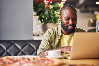 Kafede dizüstü bilgisayar kullanan neşeli Afro-Amerikalı adam.