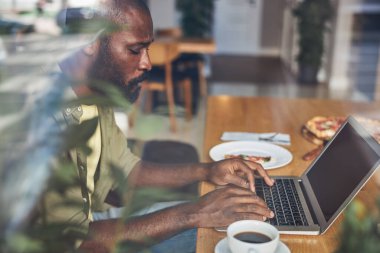Camın arkasındaki yakışıklı Afro Amerikalı dizüstü bilgisayarla çalışıyor.