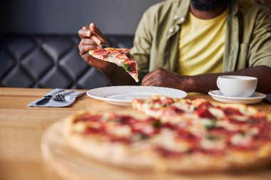 Genç adam kafede pepperonili pizza yiyor.