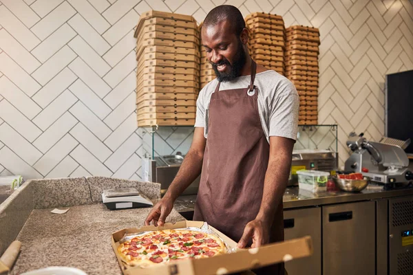 Glada ung man står vid disken med pizza — Stockfoto