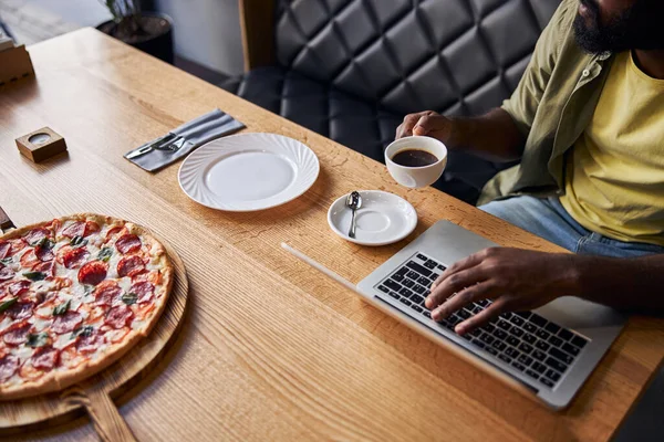 Hombre afroamericano bebiendo café y usando cuaderno en la cafetería —  Fotos de Stock