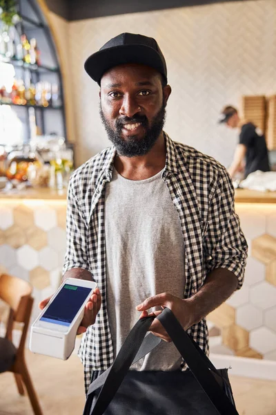 Joyful mensageiro masculino segurando saco de entrega e terminal para pagamento sem contato — Fotografia de Stock