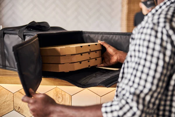 Afro americano giovane uomo mettendo scatole di pizza nella borsa di consegna — Foto Stock