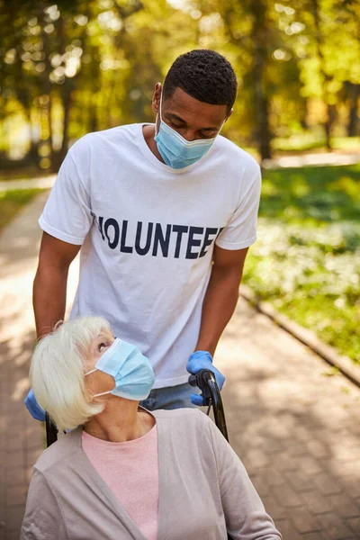Önkéntes segít egy idős felnőttnek a park vezetése közben — Stock Fotó