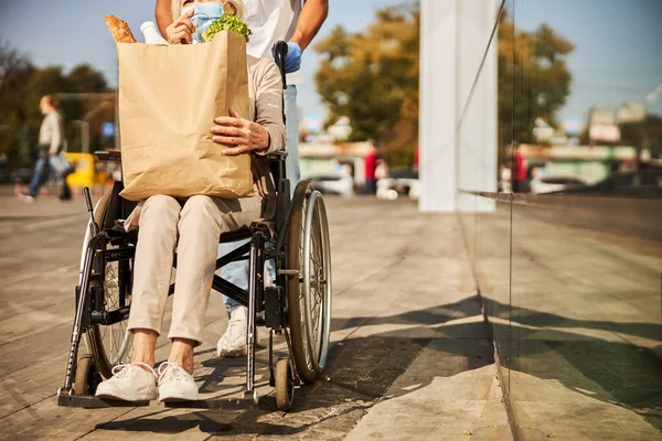 Mujer anciana en silla de ruedas que lleva un sobre de comida —  Fotos de Stock