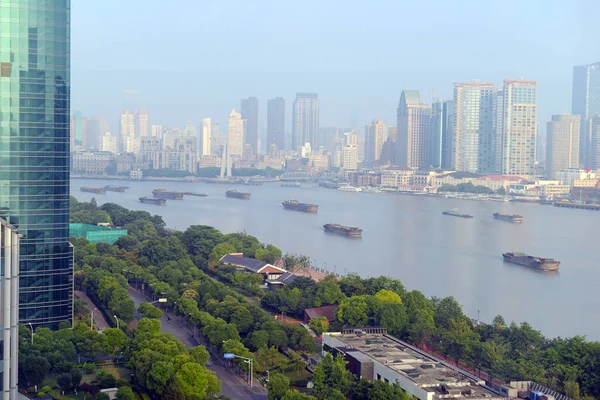 Cargo ships moving up river with city skyline background in Shanghai China, a key player in global trade manufacturing and consumer demand