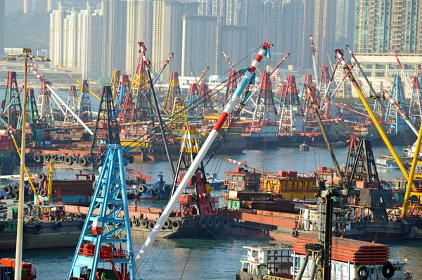 Commercial Barges with industrial freight cranes and marine shipping containers with city skyline, in Hong Kong Harbour, acting as a gateway to China