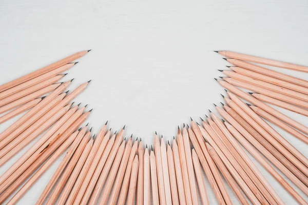 Wooden pencils arranged in a half circle on white table.