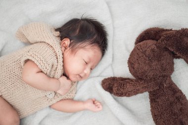 Sevimli yeni doğmuş bebek beyaz bir battaniyede kahverengi tavşan bebeğiyle huzur içinde uyuyor..