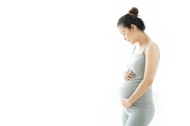 Güzel Asyalı hamile kadın gülümsüyor ve beyaz arka planda karnına dokunuyor. Hamilelik sağlıklı annelik kavramı.