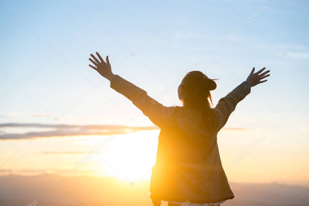 Happy woman standing alone with arms raised up during beautiful sunrise at the morning.