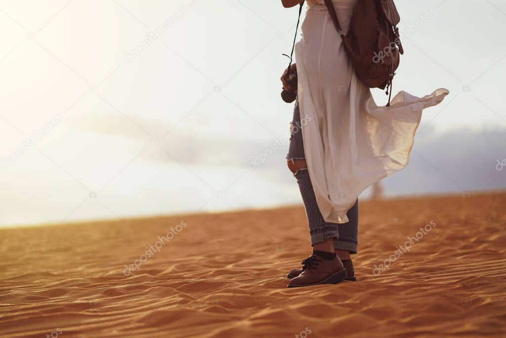 Young female exploring the desert, sandy beach with bag and camera.