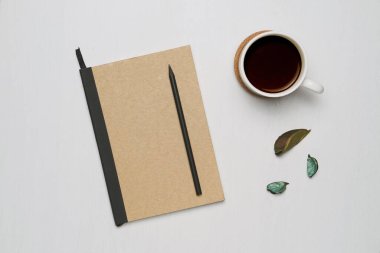 Kahverengi kaplı defterli kahve fincanı ve beyaz ahşap arka planda siyah kalem. En az düz alan, Üst Görünüm.