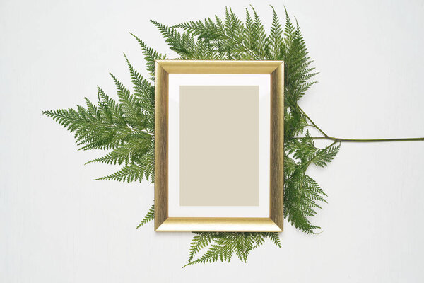 Stylish minimal composition with photo frame and green leaves on a white wooden background. Empty photo frame and green leaves. flat lay, top view.
