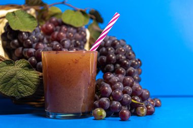 Bardakta üzüm suyu. Niagara türünün üzümleri (Vitis labrusca 'Niagara'). Mavi arka plan. Tazeleyici içecek. Niagara üzümü Brezilya 'da en çok satılan üzümlerden biridir..