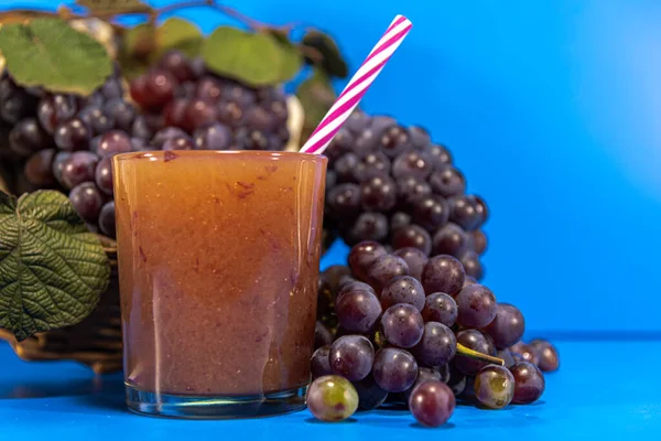 Grape juice in a glass. Bunches of grape of the niagara species (Vitis labrusca \'Niagara\'). Blue background. Refreshing drink. The niagara grape is one of the most sold grape types in Brazil.