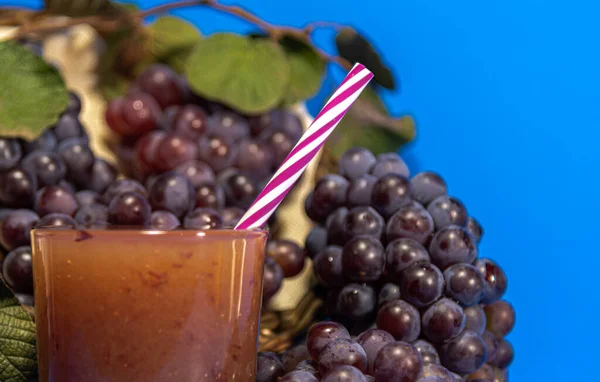 Grape juice in a glass. Bunches of grape of the niagara species (Vitis labrusca \'Niagara\'). Blue background. Refreshing drink. The niagara grape is one of the most sold grape types in Brazil.