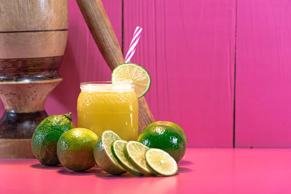 シトルス アウランティフォリア レモンジュース レモネードだ ビタミンCが豊富に含まれています ピンクの背景 さわやかな飲み物です キャピリンハを作るための木製のモルタル 木製カップ エキゾチックな飲み物 — ストック写真
