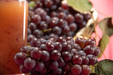 Pembe arka planda bir demet üzüm ve meyve suyu. Ferahlatıcı ve besleyici bir içecek. Meyve suyu. Vitis cinsine ait olan asmanın meyvesi. Meyve suyu ve şarap için ham madde.