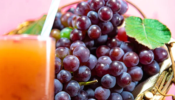 Glass of juice. Natural grape juice. pink background. Refreshing and nutritious drink. Fruit Derink. Bunches of pink grape. Fruit of the vine, which belongs to the genus Vitis. Raw material for juices and wines.