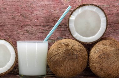 Bir bardak taze hindistan cevizi sütü. Meyveler ikiye bölünmüş ve taze. Hindistan cevizi sütü, insanlığın ana sebze kaynaklarından biri olan ve besin değeri yüksek olan hindistan cevizi meyvesinden elde edilir..