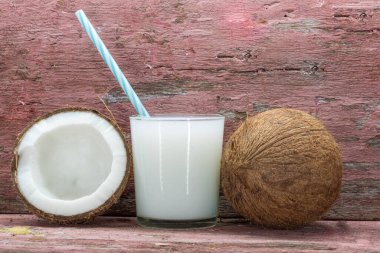 Bir bardak taze hindistan cevizi sütü. Meyveler ikiye bölünmüş ve taze. Hindistan cevizi sütü, insanlığın ana sebze kaynaklarından biri olan ve besin değeri yüksek olan hindistan cevizi meyvesinden elde edilir..