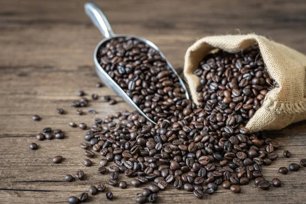 Kavrulmuş kahve çekirdekleri kumaş çanta ve kepçe, ahşap masa üzerinde kahve çekirdekleri