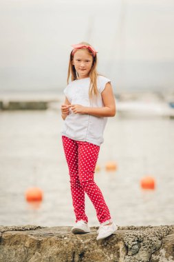 Açık havada eğleniyor, göl kıyısında güzel bir sıcak güneşli akşamı oynarken, beyaz gömlek ve ayakkabı, kırmızı puantiyeli pantolon ve kafa bandı mutlu 9 yaşında bir kız. Lake Geneva, İsviçre üzerinde alınan görüntü