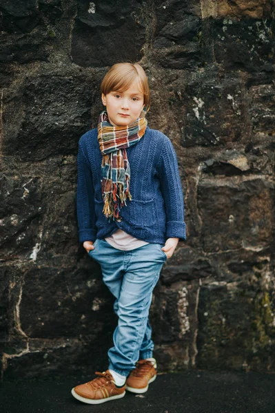 デニム ジーンズ ブルーのニット ジャケットと茶色の靴 スタイリッシュな子供を暗い壁に対してポーズを着てハンサムな男の子の屋外のポートレート 小さな子供のためのファッション — ストック写真