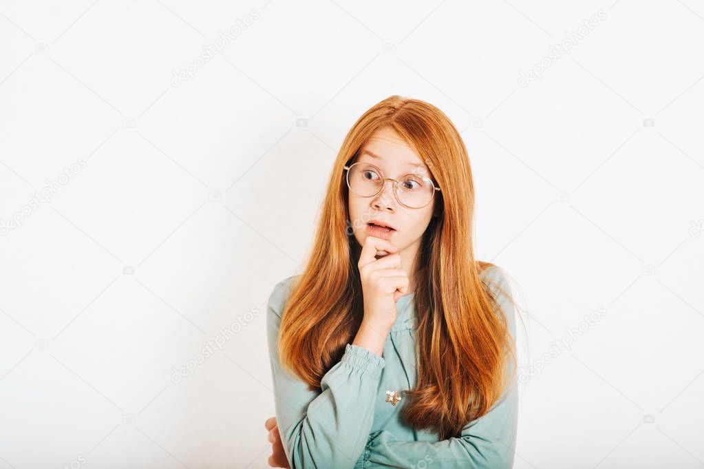 Studio shot of young preteen red-haired girl against white background, surprised facial expression